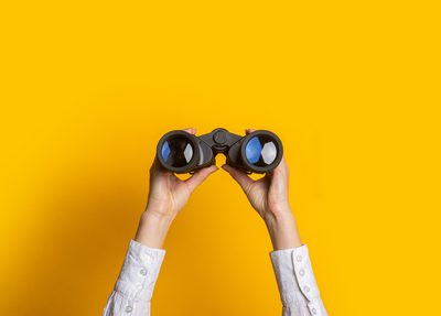 person holding binoculars up with yellow background