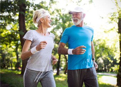 A senior woman and man running outside in nature.