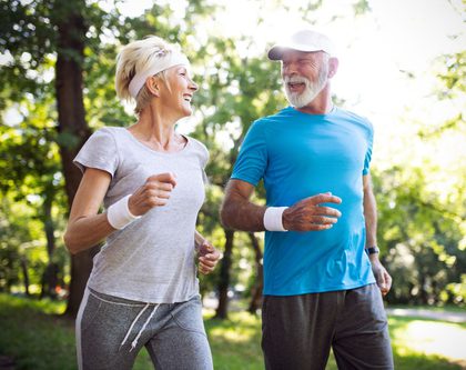 A senior woman and man running outside in nature.
