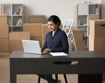woman sitting on a desk on a laptop and boxes in the background