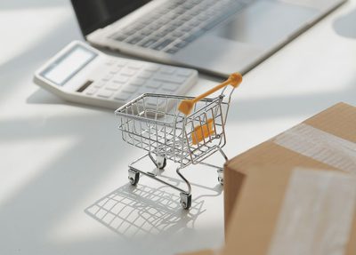 miniature shopping cart on a desk with a laptop, calculator, and cardboard boxes