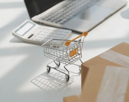 miniature shopping cart on a desk with a laptop, calculator, and cardboard boxes