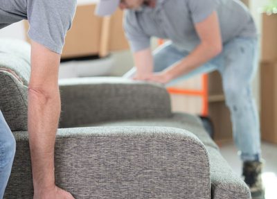 Two male workers carrying a gray couch