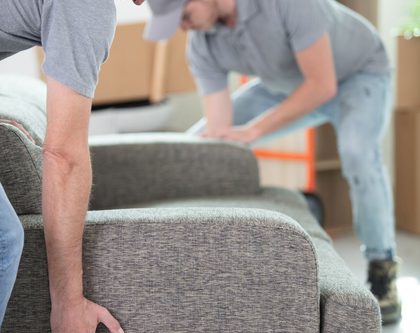 Two male workers carrying a gray couch