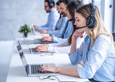 group of employees on laptops at a desk with headphones