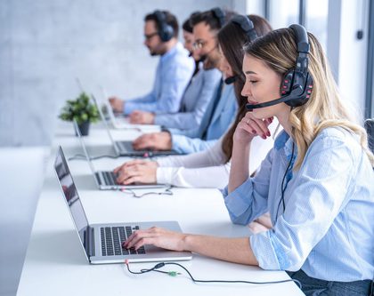 group of employees on laptops at a desk with headphones