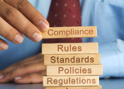 a man stacking blocks that say "compliance, rules, standards, policies, regulations, law"