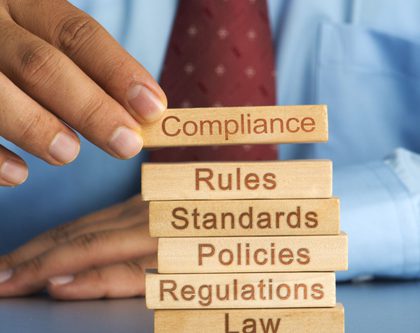 a man stacking blocks that say "compliance, rules, standards, policies, regulations, law"