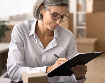 a woman wearing glasses writes notes on a clipboard