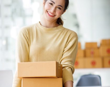 a woman stands in an office, balancing a stack of boxes in her arms