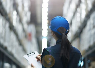 a woman stands in a warehouse, holding a clipboard and reviewing inventory amidst shelves of stored items