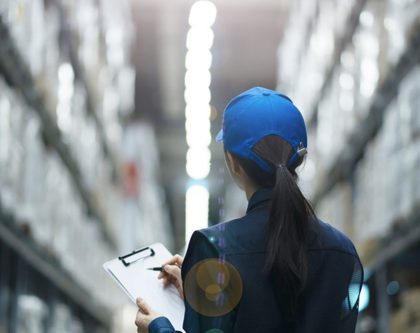 a woman stands in a warehouse, holding a clipboard and reviewing inventory amidst shelves of stored items