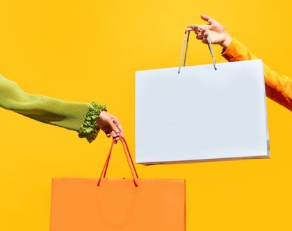 two women with shopping bags stand on a bright yellow background
