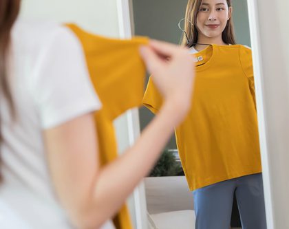 woman holding yellow t-shirt in front of mirror
