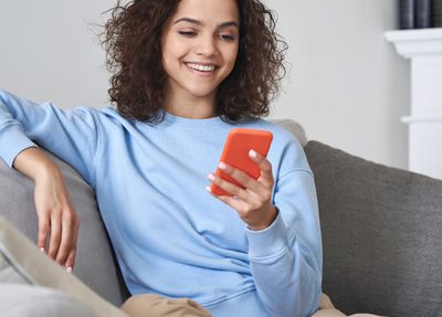 woman smiling, holding phone, sitting on couch