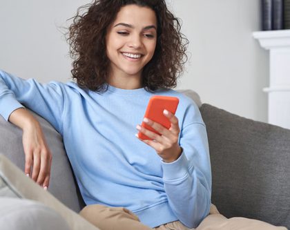 woman smiling, holding phone, sitting on couch