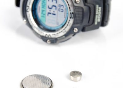 wrist watch and coin and button batteries against a white background