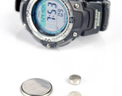 wrist watch and coin and button batteries against a white background