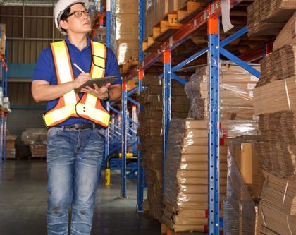 a man stands in a warehouse, holding a clipboard and reviewing inventory