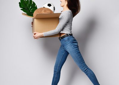 woman jumping and holding a cardboard box containing various items including a plant and a soccer ball