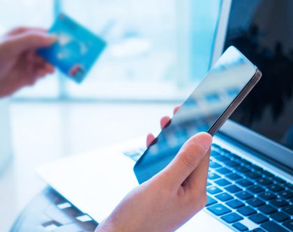 A woman holding a mobile phone and shopping online on a laptop