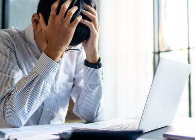 a man sits at a desk, resting his head in his hands, conveying a sense of frustration