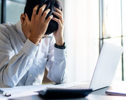 a man sits at a desk, resting his head in his hands, conveying a sense of frustration