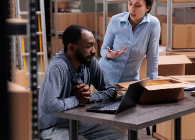 two individuals collaborating on tasks inside a warehouse, surrounded by shelves and boxes