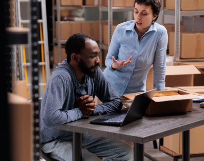 two individuals collaborating on tasks inside a warehouse, surrounded by shelves and boxes