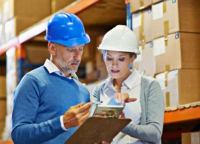 a man and woman in a warehouse reviewing a clipboard