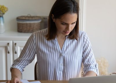 woman sitting at a desk focused on her laptop with scattered papers