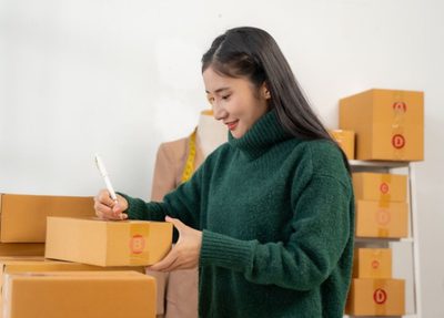 woman writing on a box in a room surrounded by shipments