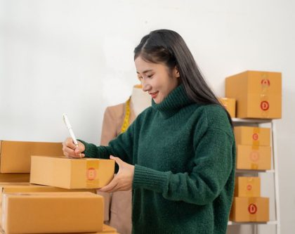 woman writing on a box in a room surrounded by shipments