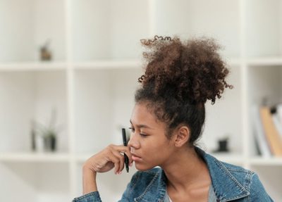 woman sits at desk in office setting looking at laptop with documents in hand