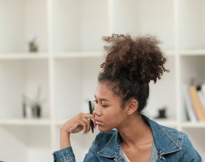 woman sits at desk in office setting looking at laptop with documents in hand