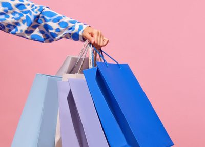 woman holding colorful shopping bags against a vibrant pink background