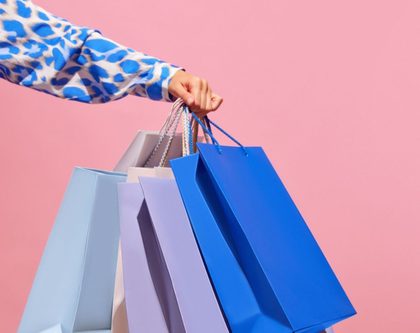 woman holding colorful shopping bags against a vibrant pink background